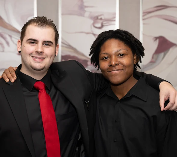 Two friends in formal attire embracing and facing the camera