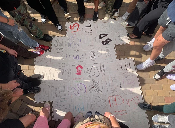 Teens standing with only feet visible near their art tiles put together like a puzzle