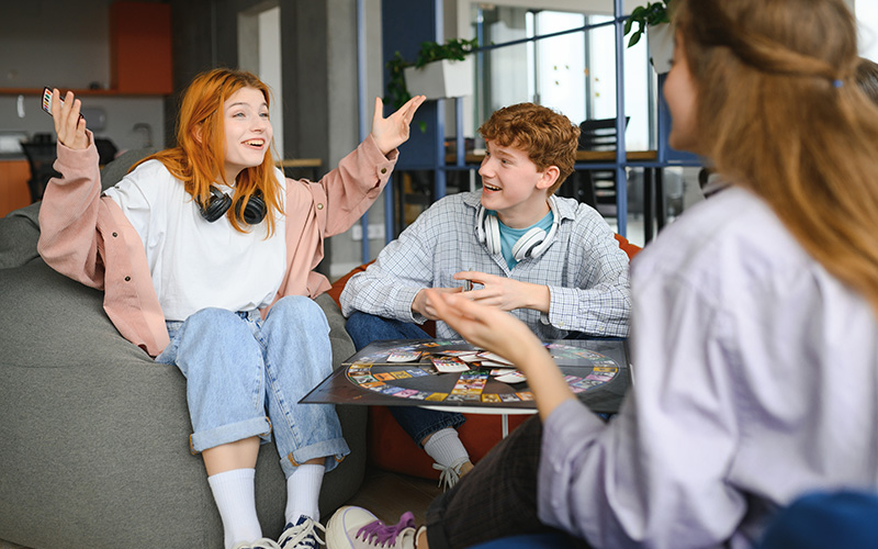 Group of creative friends sitting at wooden table. People having fun while playing board game.